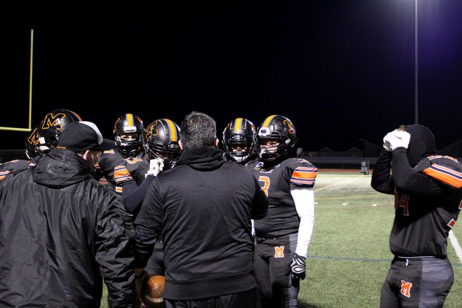 Coaches consult captain Paul Zunkel and other players on the varsity football team from the sidelines during their first game of the season on March 19 at Huntley High School.