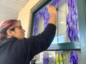 A student from Art Club paints a window at Green Street Cafe on Sept. 29 in preparation for Homecoming next week.