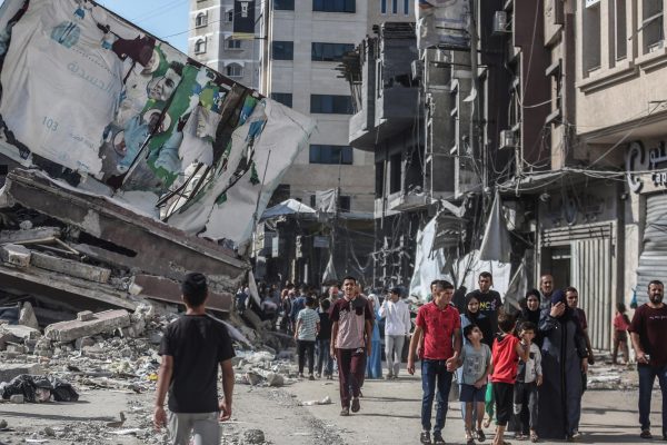 Palestinians walk past the remains of buildings destroyed by Israeli airstrikes, on Oct. 16, 2023, in Palestinian Territories, Khan Yunis. Hundreds of thousands of Palestinians flee to the south of the Gaza Strip to avoid an expected Israeli ground invasion, essential supplies are running out, according to UNÂ workers. 